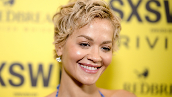Rita Ora smiling against a yellow background